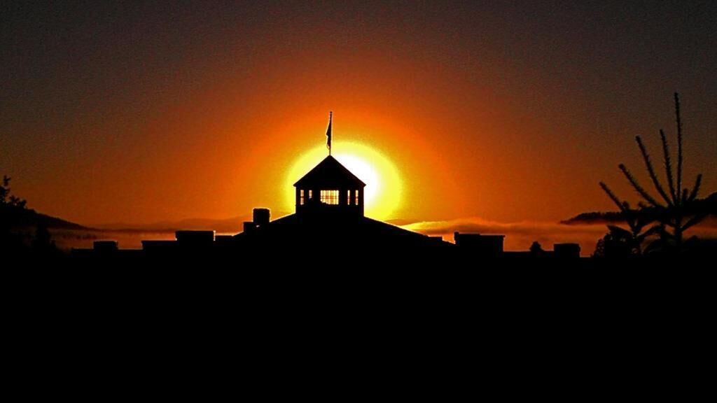 La silhouette d’un bâtiment surmonté d’un drapeau, se détachant sur un coucher de soleil.