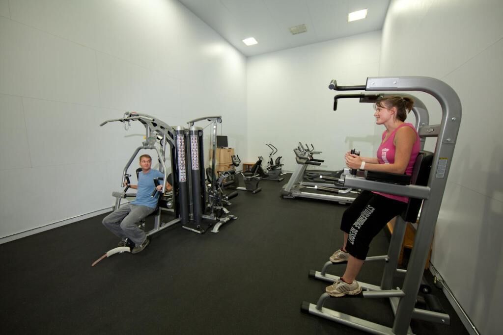 A gym with various exercise machines, including a seated row machine and a leg press.