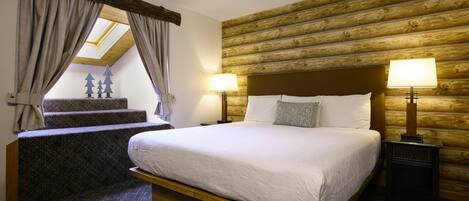 A bedroom with a wooden headboard, a large bed, two bedside lamps, and a view of a staircase with a skylight.
