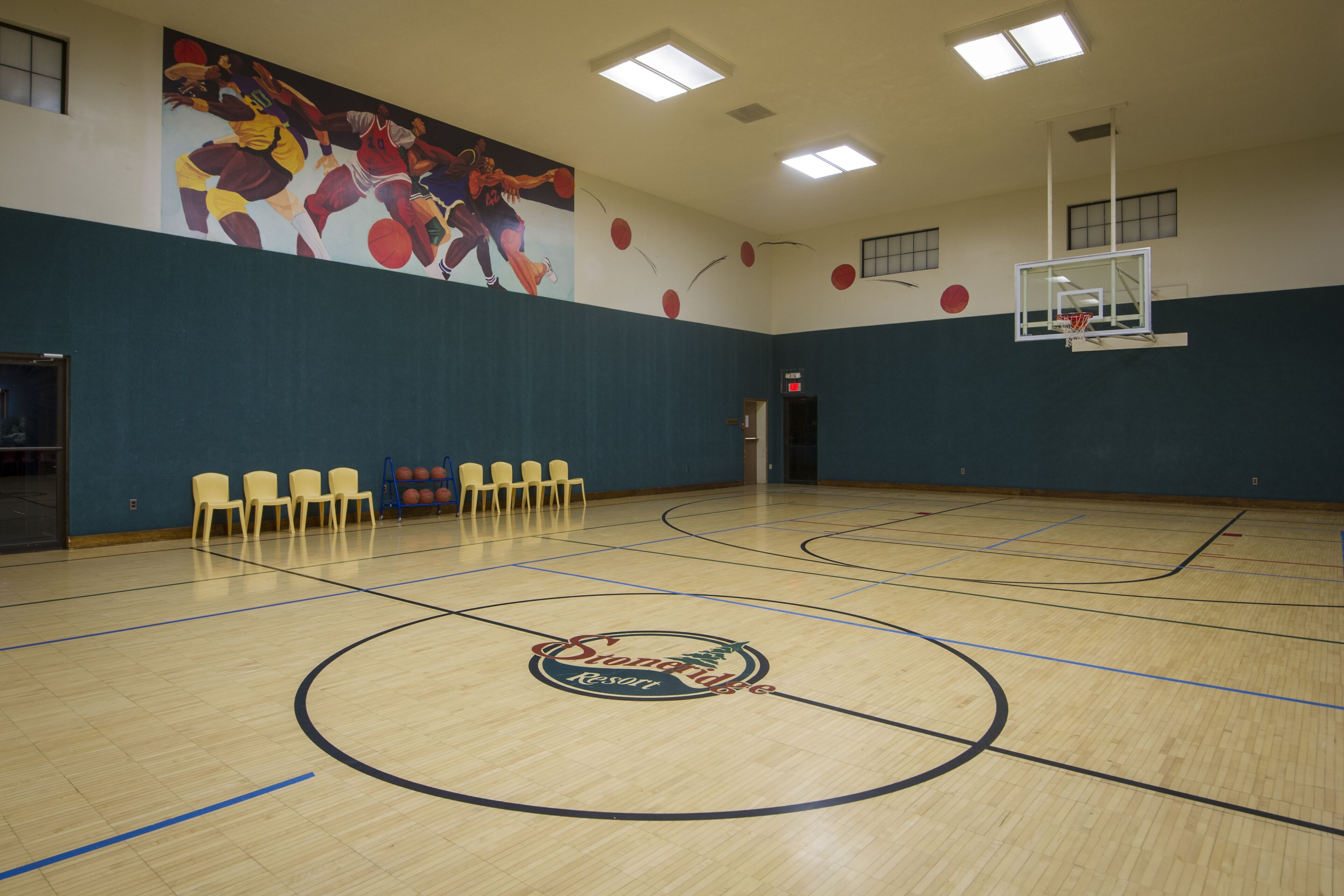 A basketball court with a mural, chairs, and a basketball hoop.