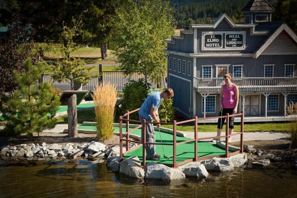 A miniature golf course with a bridge over water, a sign for St. Elmo Hotel, and a dining area.