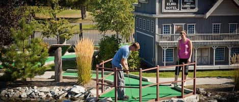 A miniature golf course with a bridge over water, a sign for St. Elmo Hotel, and a dining area.