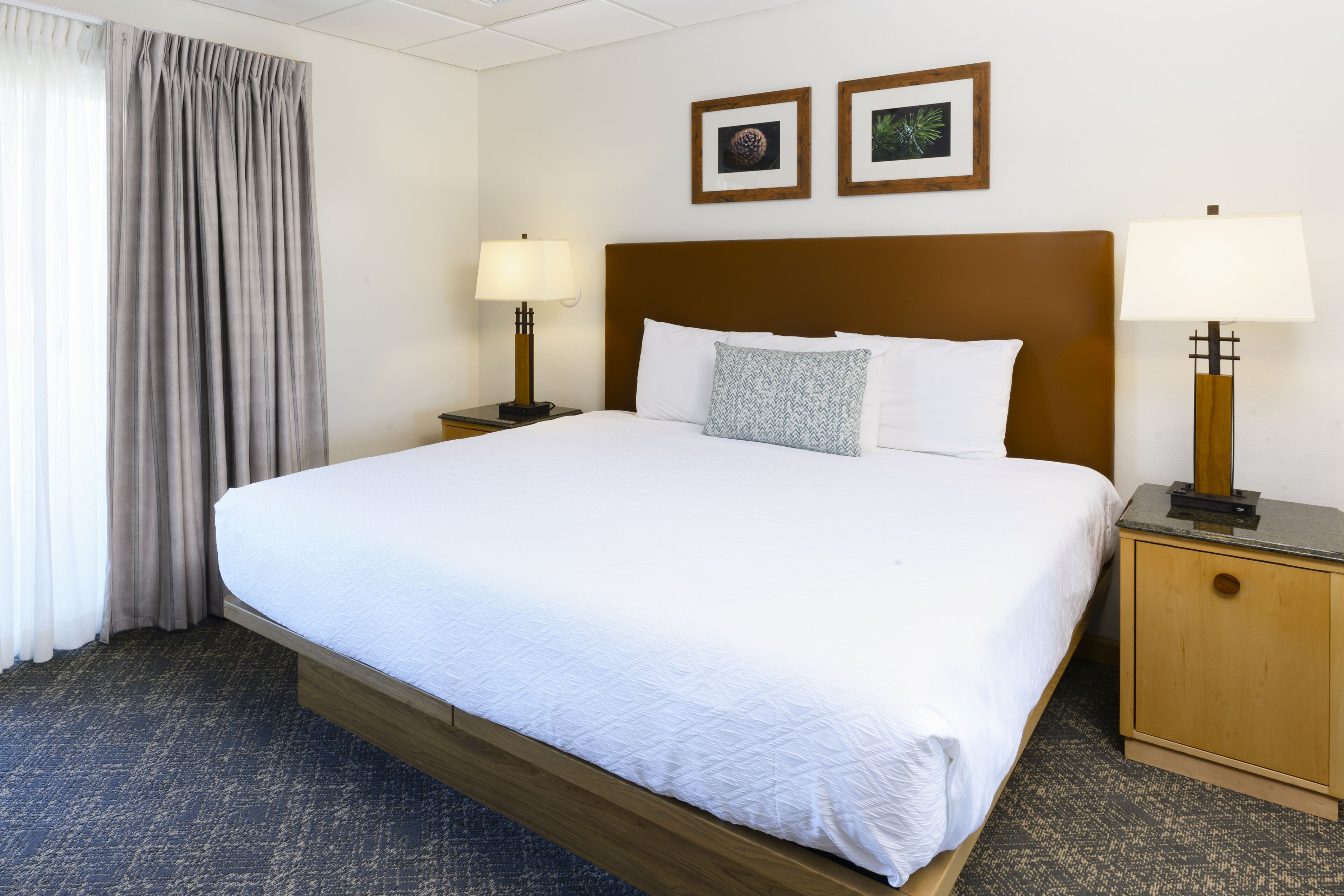 Hotellihuone, jossa on suuri sänky, kaksi yöpöytää valaisimineen, puinen sängynpääty ja kaksi kehystettyä kuvaa seinällä.