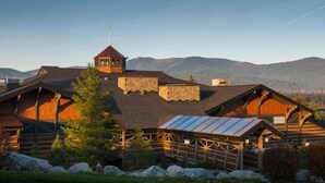 A log cabin-style building with a central tower, multiple rooms with sloped roofs, and a covered outdoor area with a metal roof. - Stoneridge Resort (Blanchard)