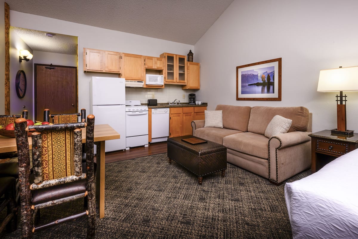 A compact hotel room with a kitchenette, a sofa, a small table, and a bed.