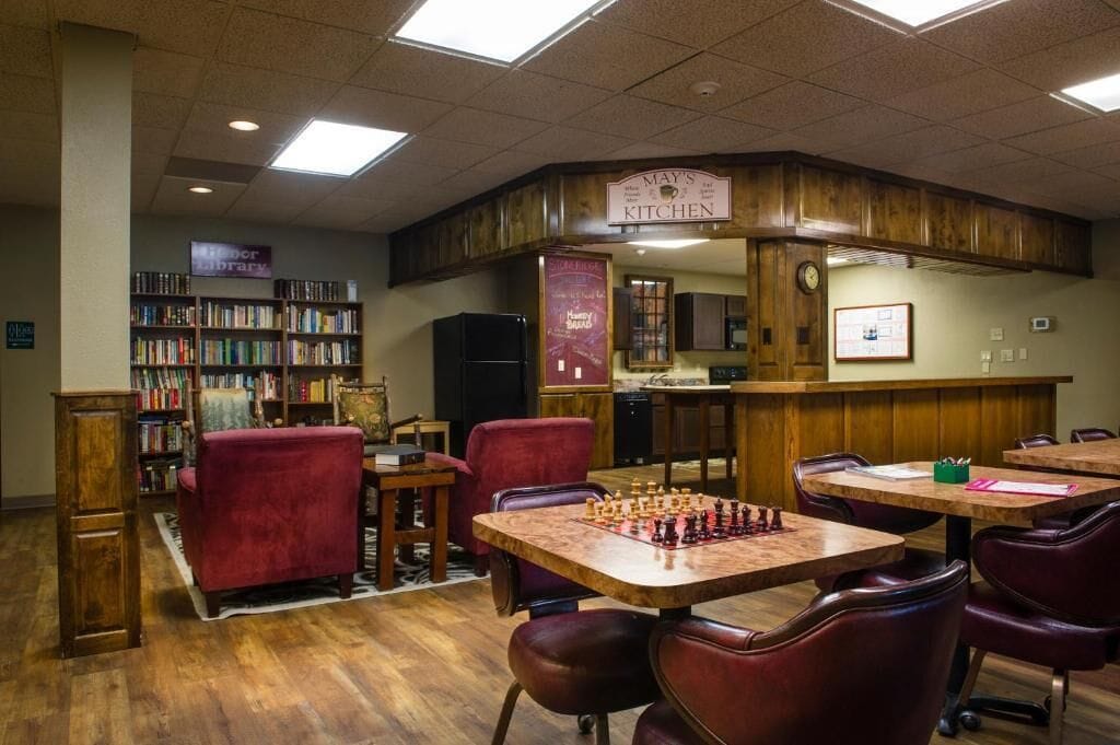 A library with bookshelves, a chess table, and a kitchen area.