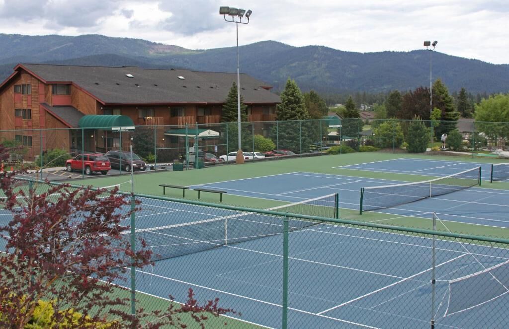 Un complexe de courts de tennis comprenant plusieurs terrains, un bâtiment doté d’un toit végétalisé et des montagnes en arrière-plan.