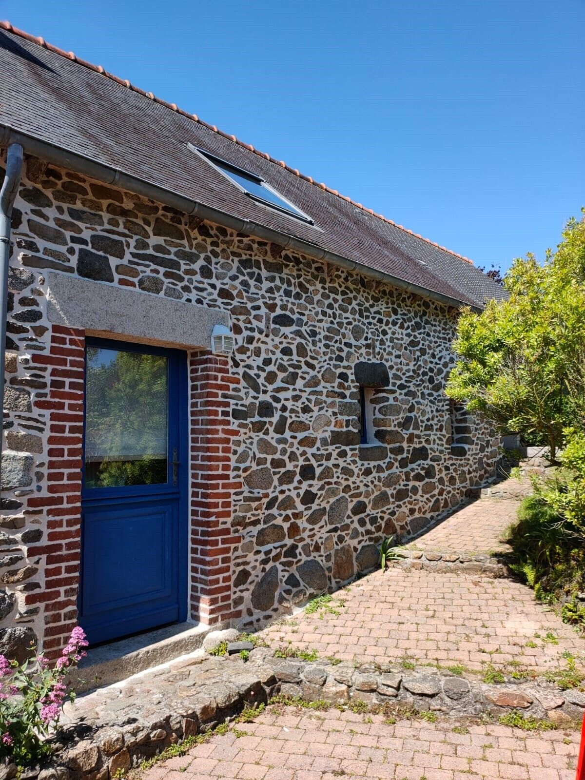 Een gebouw van steen met een blauwe deur, een pannendak en een bakstenen muur.