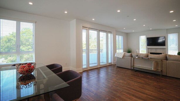 A spacious living room with a glass dining table, dark wood flooring, a beige sofa, and a flat-screen TV mounted on the wall. - Beverly Hills Luxury Condo, 5% Discounts on monthly bookings. (Los Angeles)
