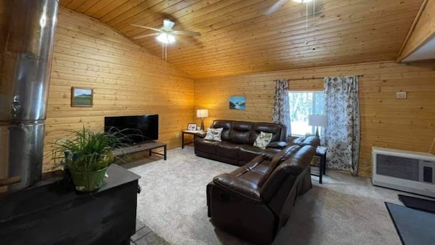 A cozy cabin interior with a wooden ceiling, a fireplace, a sofa, a television, and a large window with curtains. - Willow Forest Cabin with Sauna, Pet and Family Friendly (Willow)