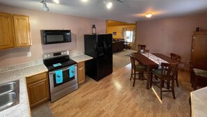 A compact kitchen with a microwave, stove, refrigerator, and a dining area with a table and chairs. - Willow Forest Cabin with Sauna, Pet and Family Friendly (Willow)