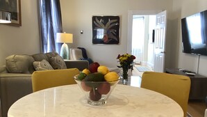 A modern living room with a round marble table, yellow chairs, a sofa, and a dining table with a fruit bowl. - Exquisite 3rd Floor Private Apt with Style (Westfield)