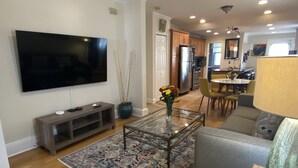 A modern living room with a flat-screen TV, a coffee table, a sofa, and a dining area with chairs and a table. - Exquisite 3rd Floor Private Apt with Style (Westfield)
