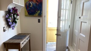 A hallway with a wooden floor, a round rug, a desk with drawers, a wall-mounted wreath, and a painting. - Exquisite 3rd Floor Private Apt with Style (Westfield)