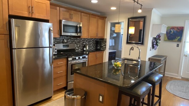 A modern kitchen with stainless steel appliances, wooden cabinets, and a central island with bar stools. - Exquisite 3rd Floor Private Apt with Style (Westfield)