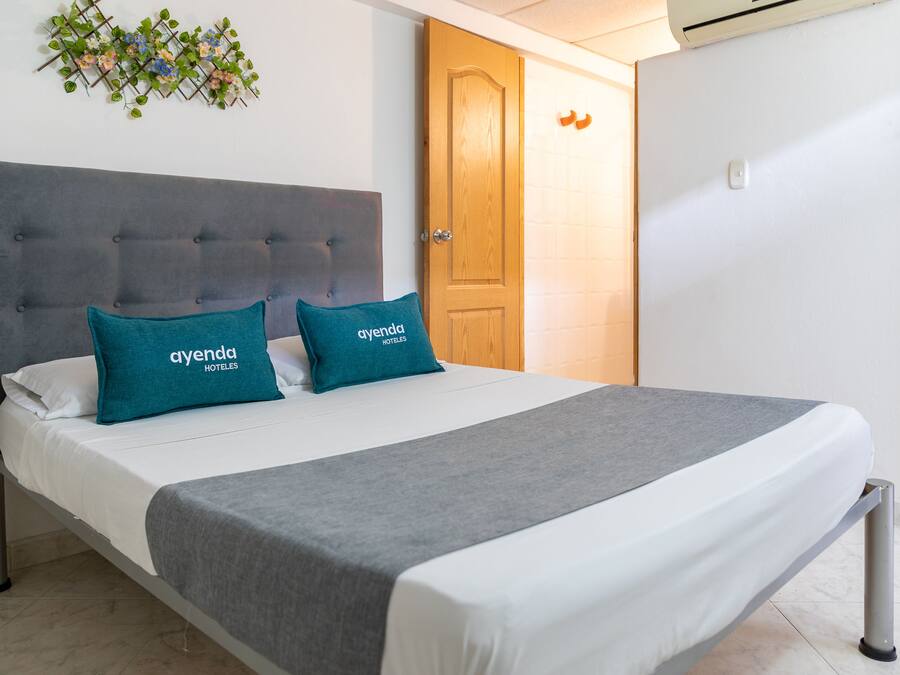 A neatly made bed with two pillows, a grey headboard, and a white wall with a decorative plant.