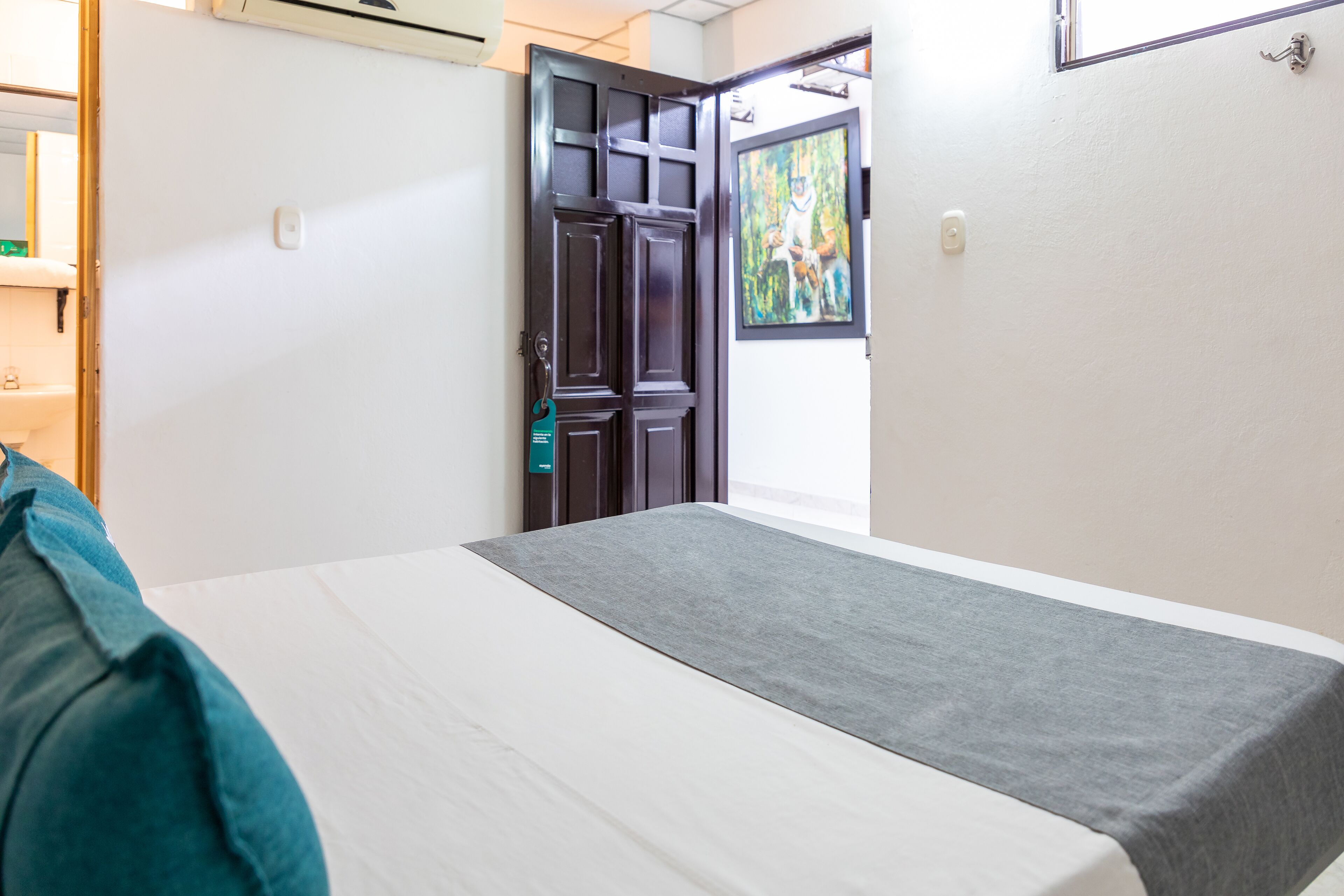 A hotel room with a bed, a door, and a painting on the wall.