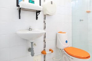 Une salle de bain avec un lavabo blanc, des toilettes avec un abattant orange et un distributeur de savon.