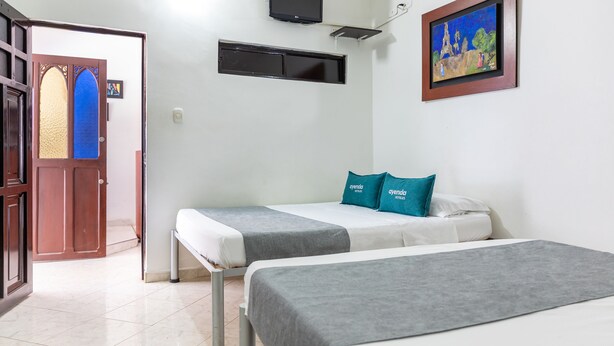 Une chambre d’hôtel avec deux lits, une porte, une fenêtre, un tableau et un téléviseur fixé au mur.