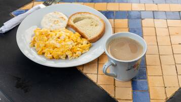Ein Teller mit Rührei, Toast und einer Tasse Kaffee auf einer gefliesten Tischplatte.