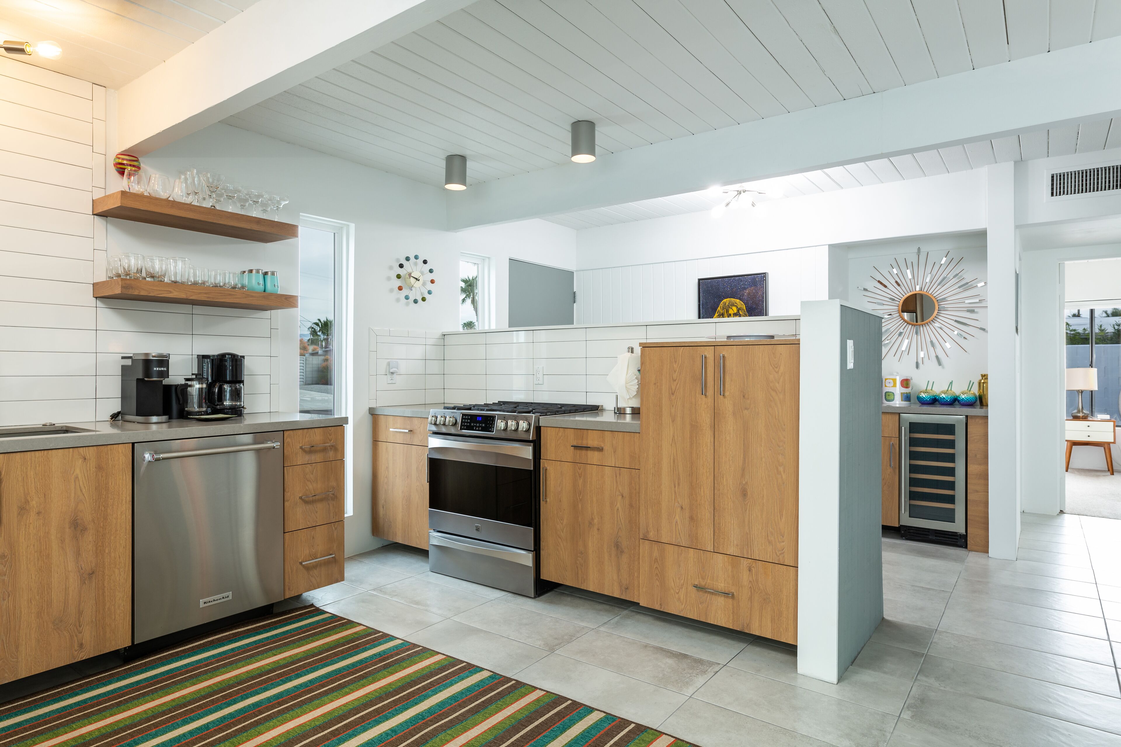 A modern kitchen with wooden cabinets, stainless steel appliances, and a striped rug.