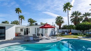 A swimming pool with lounge chairs and a red umbrella, surrounded by palm trees and a modern building. - Racquet Club Escape (Palm Springs)