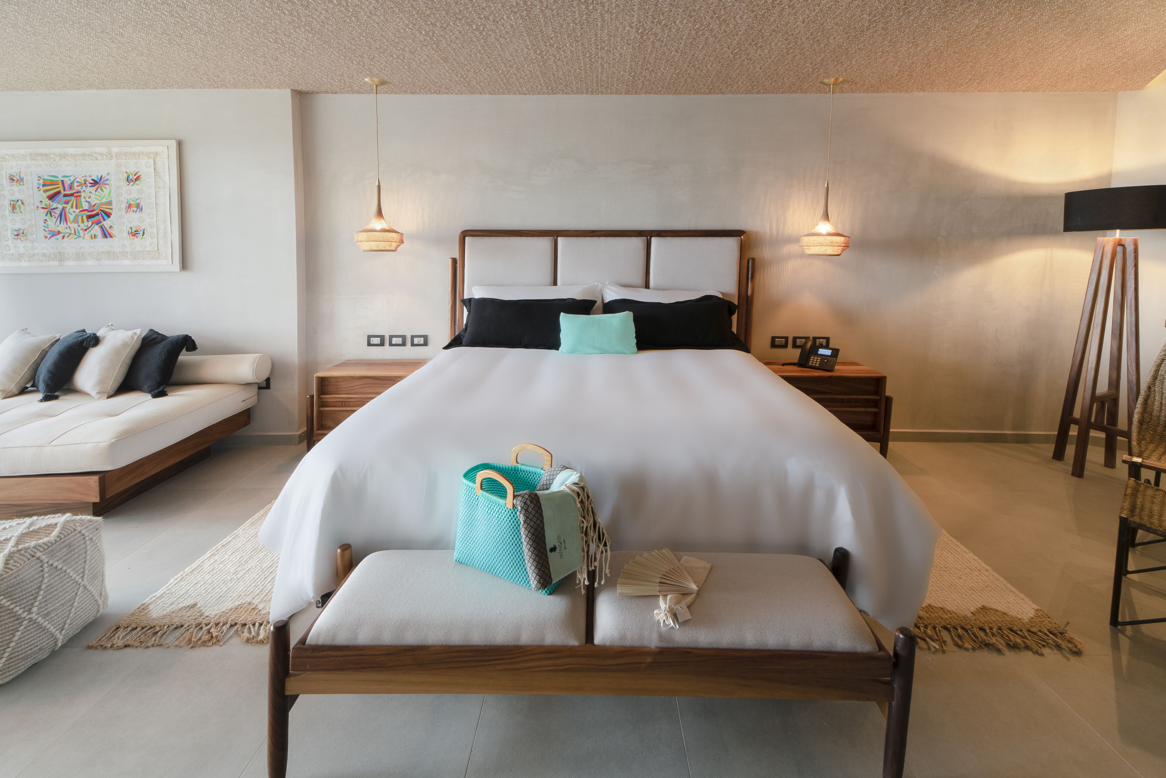 Une chambre à coucher bien aménagée, avec un grand lit, des tables de chevet, un banc et une œuvre d’art accrochée au mur.