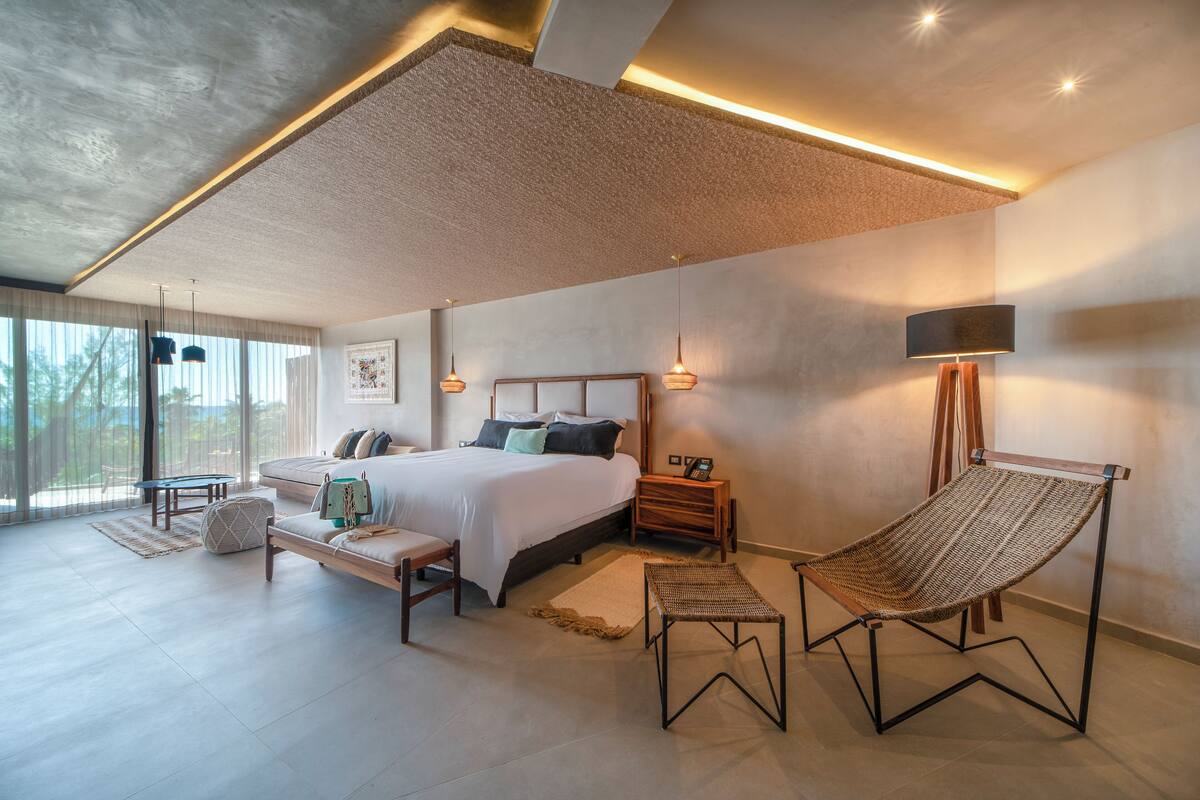Une chambre à coucher moderne avec un grand lit, des tables de chevet, un fauteuil suspendu et une vue sur l’extérieur.