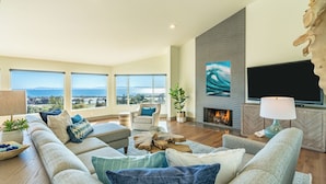 A spacious living room with a fireplace, large windows, and a view of the ocean.