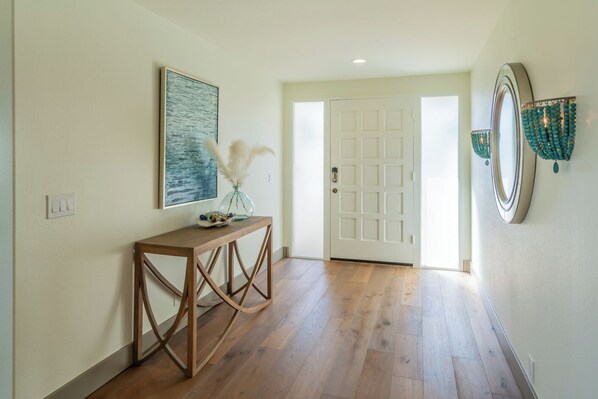 A hallway with a wooden floor, a white door, a framed painting, and a decorative mirror.