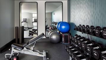 Un gimnasio con equipo de ejercicio, incluyendo cintas de correr, mancuernas y pelotas de ejercicio.