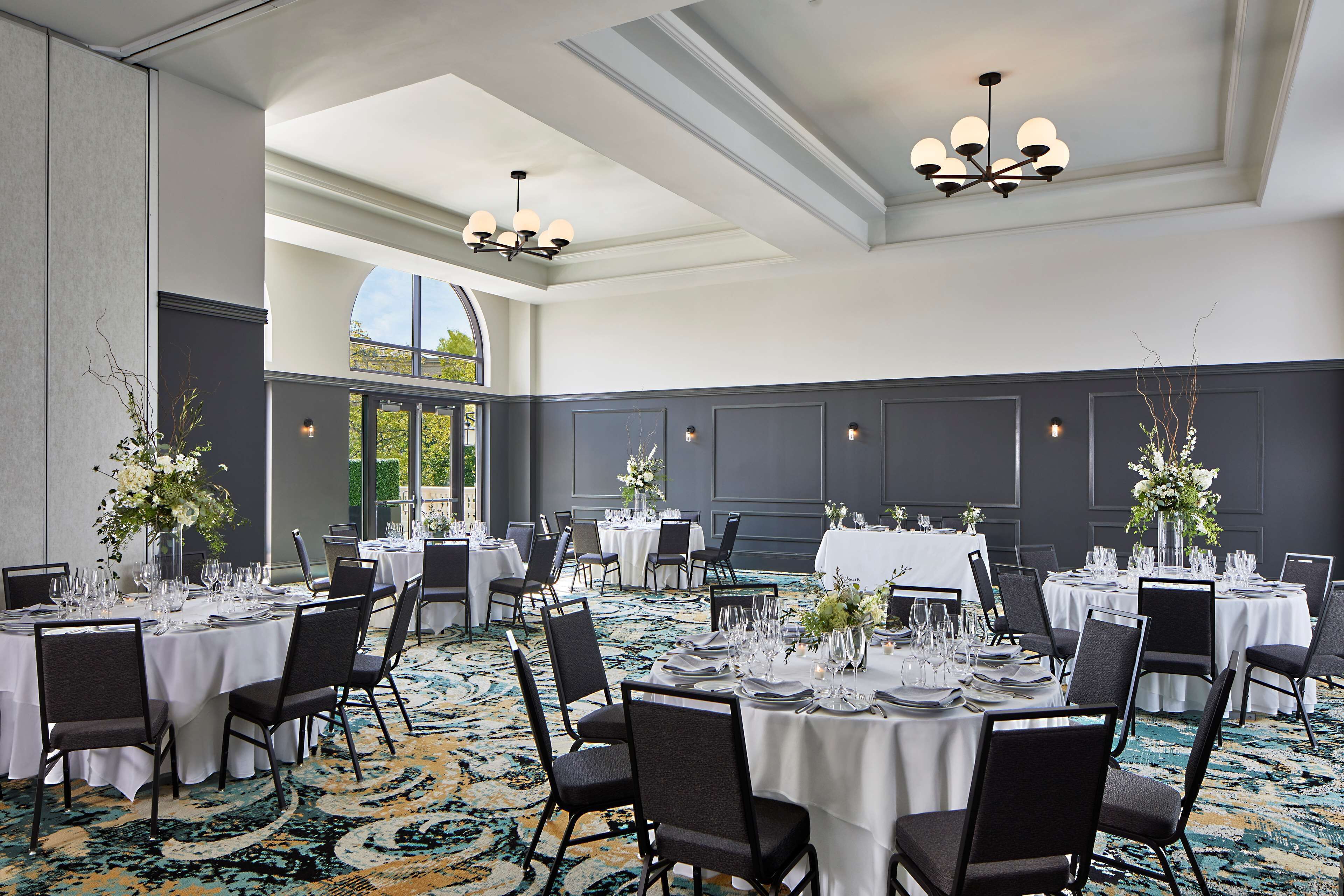 Une salle de banquet avec des tables rondes dressées pour le repas, agrémentées de nappes blanches et de chaises noires.