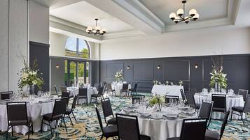 Une salle de banquet avec des tables rondes dressées pour le repas, agrémentées de nappes blanches et de chaises noires.