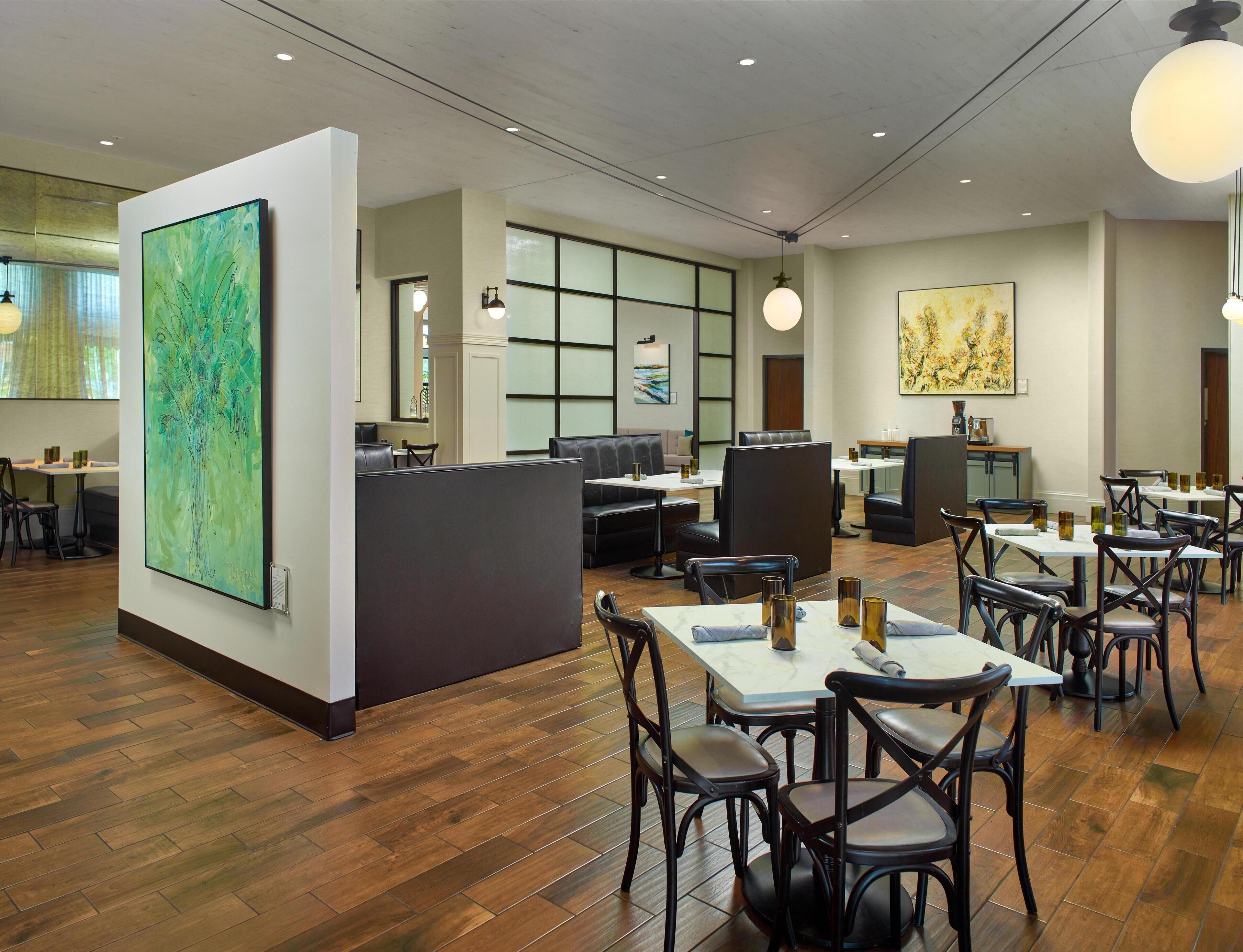A modern restaurant with wooden flooring, black leather seating, and artwork on the walls.