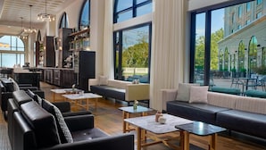 A spacious lounge area with leather sofas, wooden tables, and large windows offering views of the outdoor seating area.
