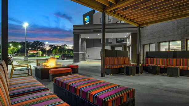 Un espacio al aire libre con cojines a rayas de colores, una chimenea y vistas a la calle al atardecer.