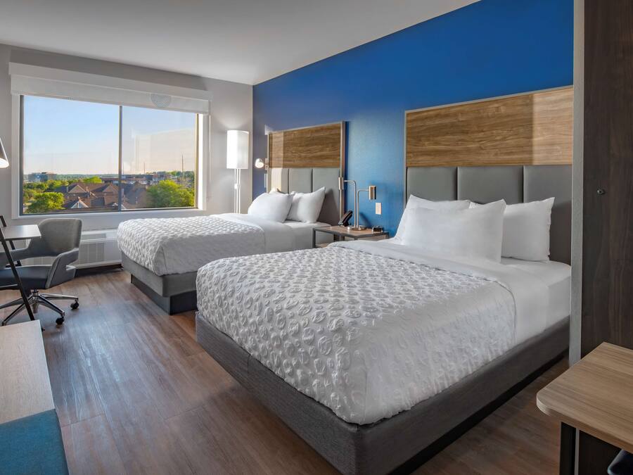 A hotel room with two beds, a desk, and a chair.