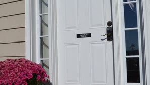 A white front door with a nameplate, a large potted plant, a small pumpkin, and a welcome mat. - Gipfel Suite - Himmel Haus Bed & Breakfast (Hermann)