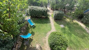 Un jardin avec un chemin dallé, deux fauteuils de jardin bleus et des arbustes soigneusement taillés.