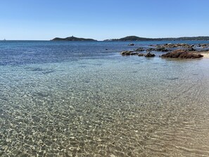 Una playa costera despejada con costa rocosa y colinas al fondo.