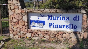 Un mur de pierres sur lequel est apposée une plaque indiquant « Marina di Pinarello » et sur laquelle est représentée une illustration de bateau.