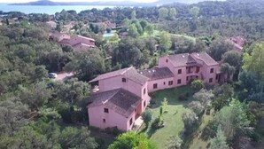 Une vue aérienne d’un vaste domaine comprenant plusieurs bâtiments, entouré d’une végétation luxuriante et avec un lac en arrière-plan.