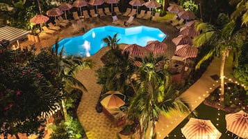 A pool area with lounge chairs and umbrellas, surrounded by palm trees and greenery.