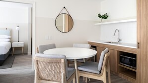 A modern kitchen with a round dining table, wicker chairs, a hanging mirror, and a built-in microwave.
