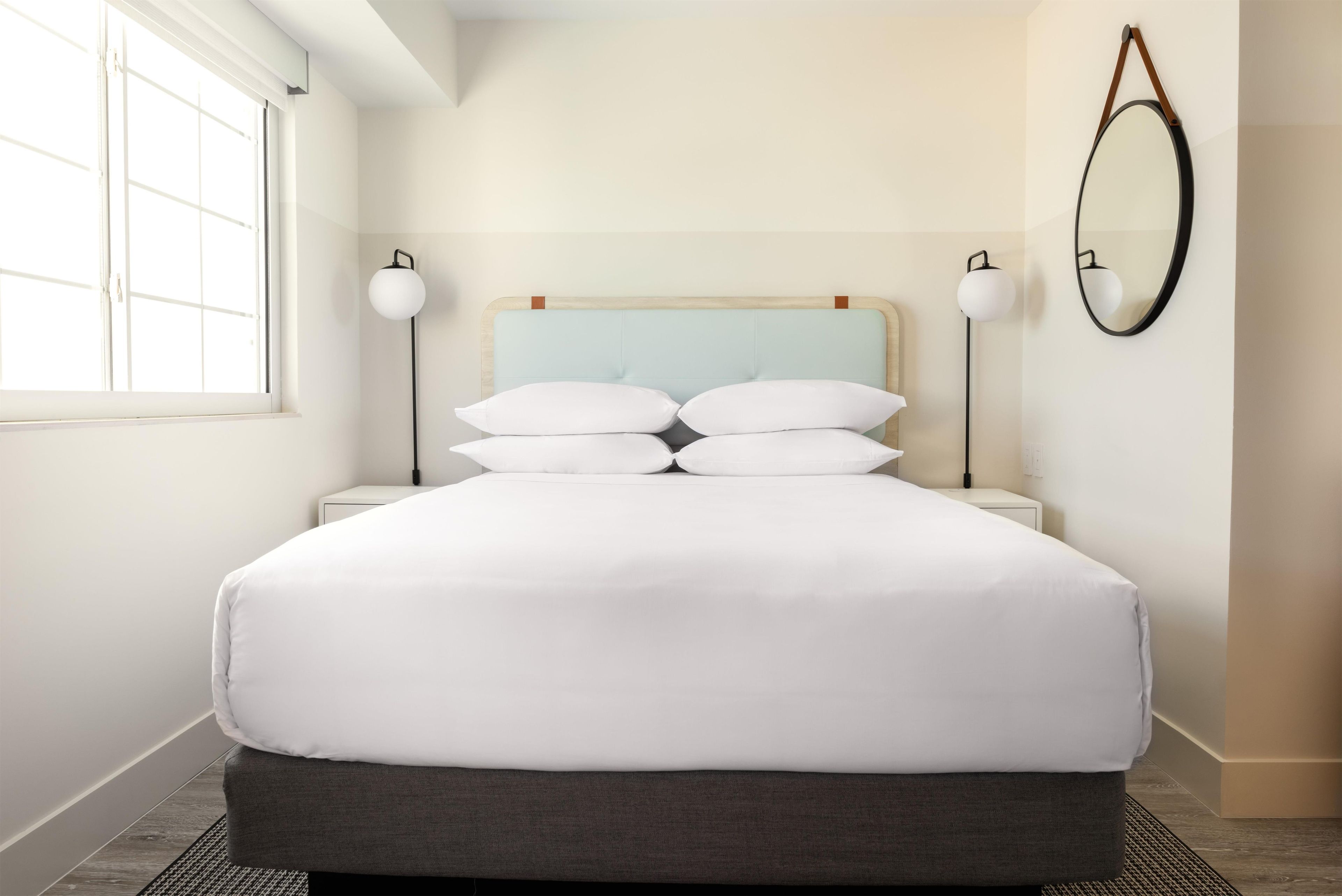 A neatly made bed with white linens, a light blue headboard, and two bedside lamps.