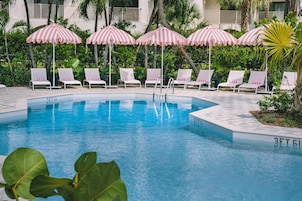 Piscina com espreguiçadeiras brancas e guarda-sóis listrados de rosa.