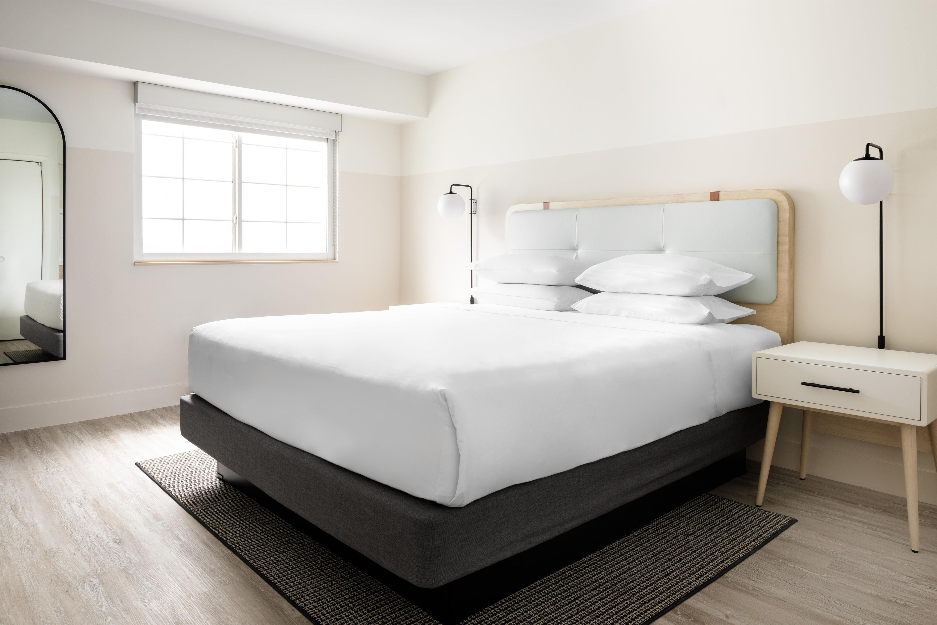 Ein modernes Schlafzimmer mit einem großen Bett, Nachttischen, einem Spiegel und einem Fenster.