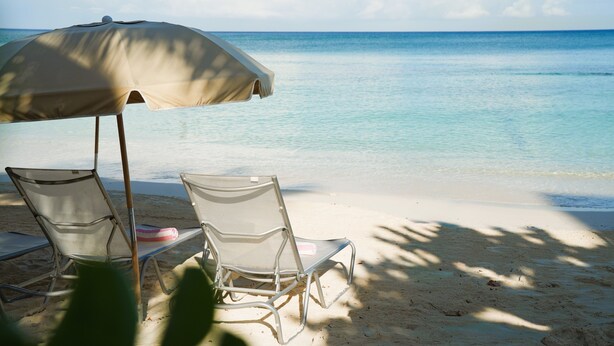 A beach with two lounge chairs and a beach umbrella.