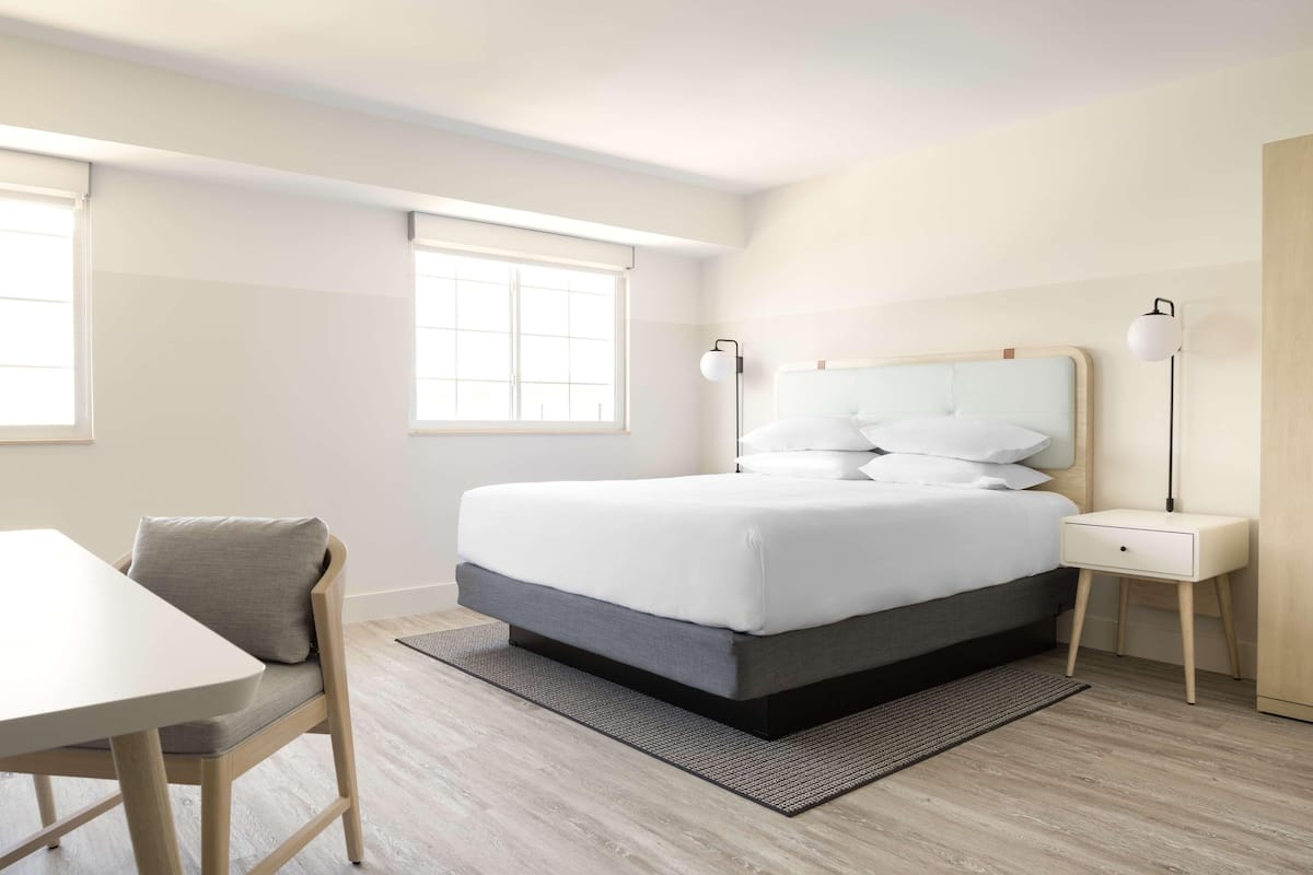 A neatly arranged bedroom with a bed, bedside tables, a chair, and a window.
