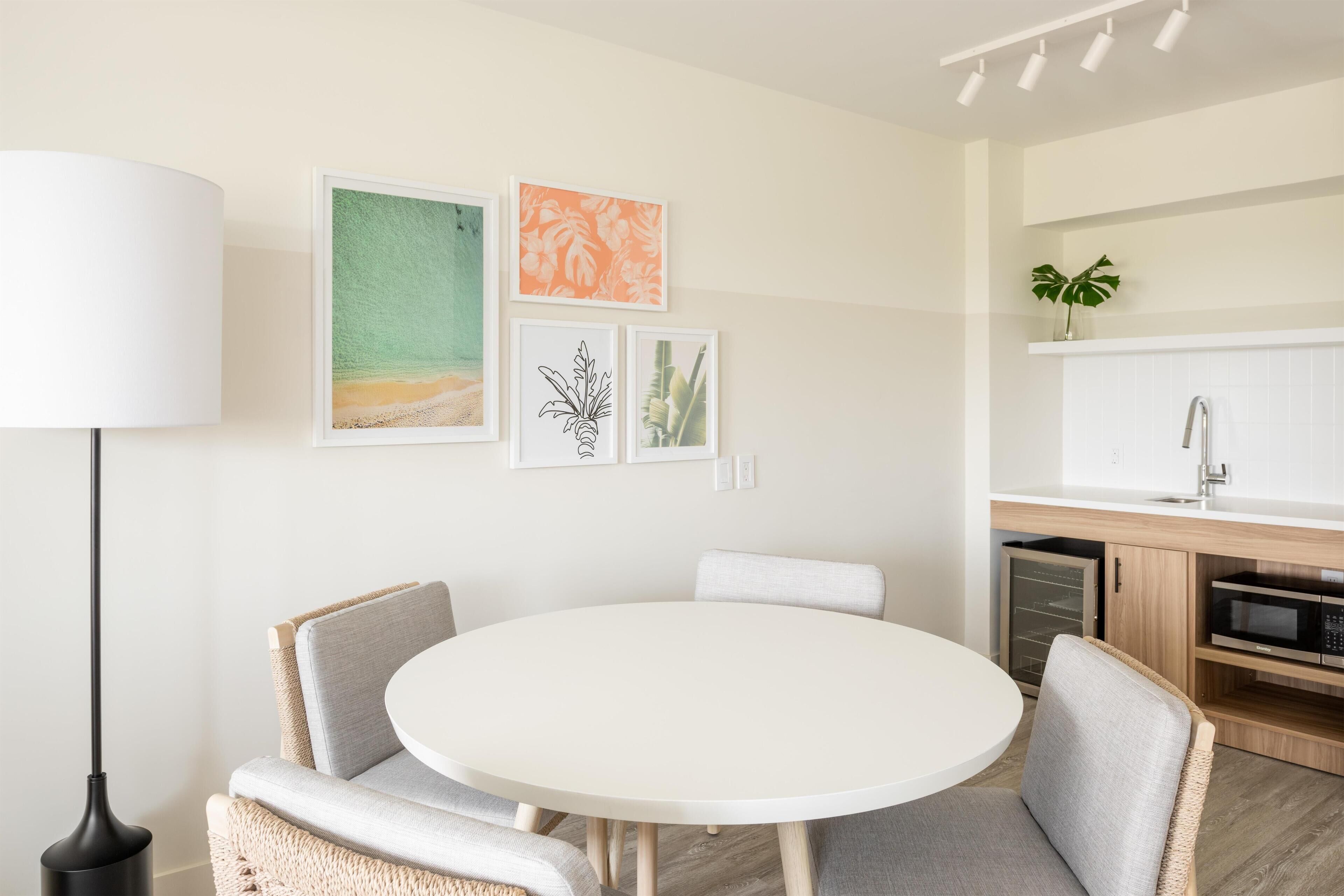 A modern kitchen with white cabinets, a microwave, and a sink. There is a round dining table with chairs and a floor lamp.